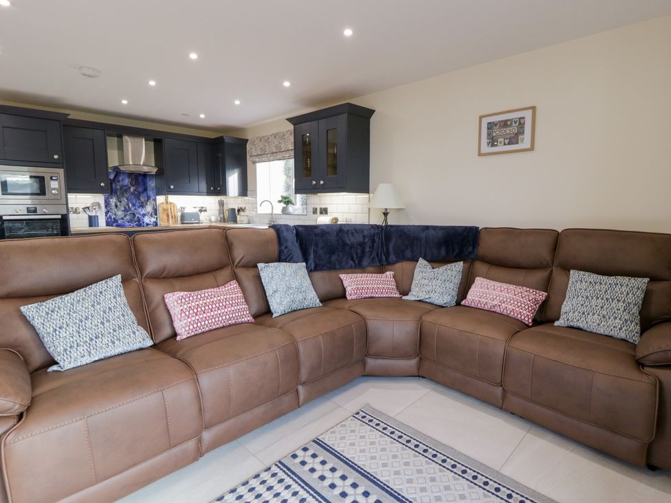 A living room with a brown sofa and kitchen cabinets at Beudy near Llanilar