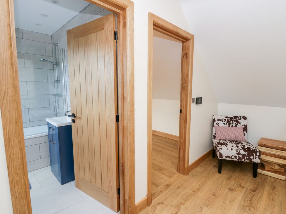 A bathroom with a bathtub and shower, and a chair outside at Beudy near Llanilar