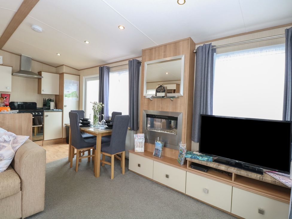 A living room with a sofa, dining table and television at Seashell Lodge, 50 Foxburrow Hang, Belton, Norfolk