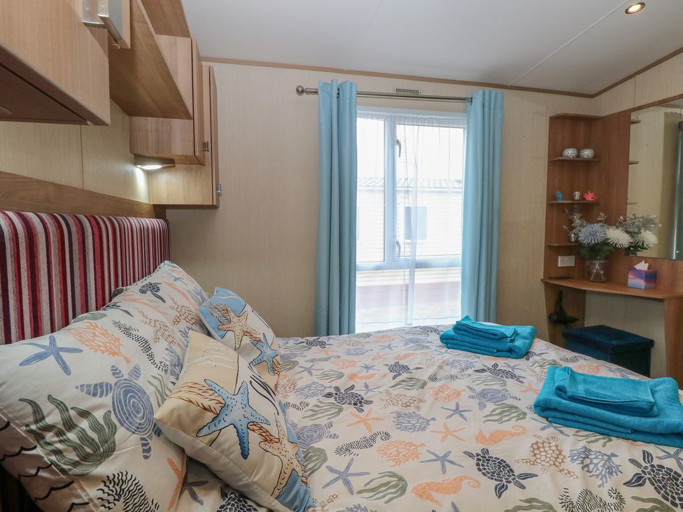 A bedroom with a bed and window at Seashell Lodge, 50 Foxburrow Hang, Belton, Norfolk
