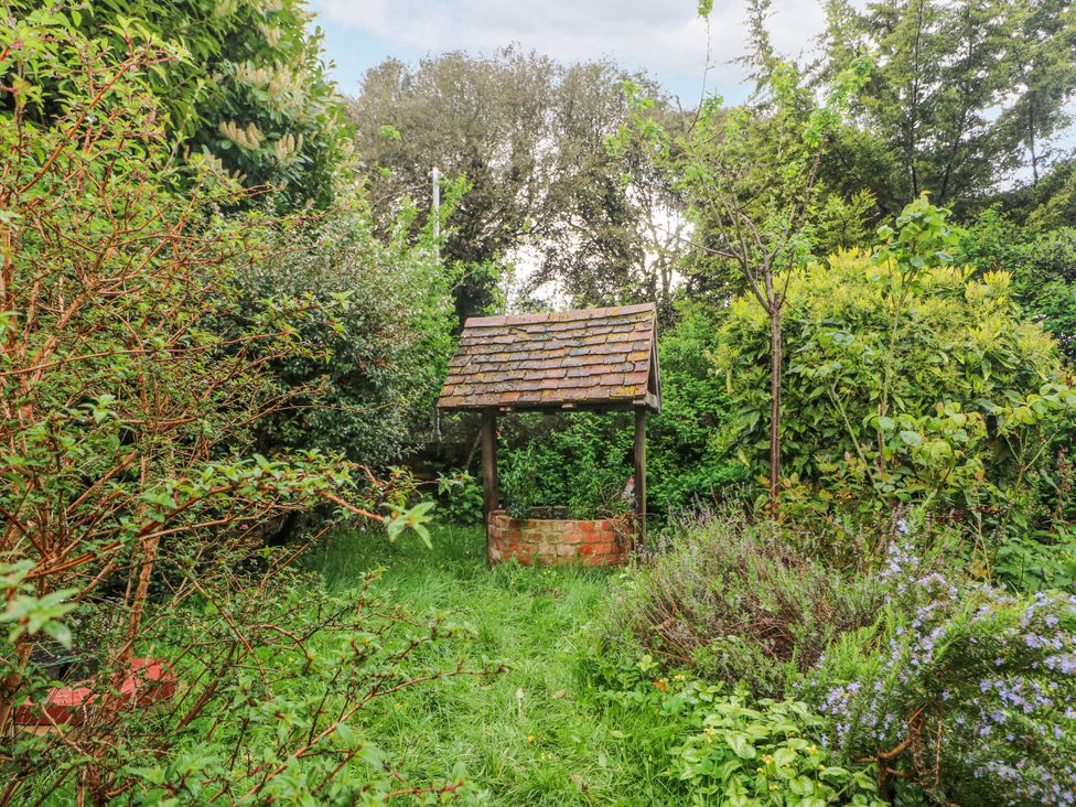 A garden with a brick well surrounded by grass and shrubs at Chilton Manor House in Sittingbourne