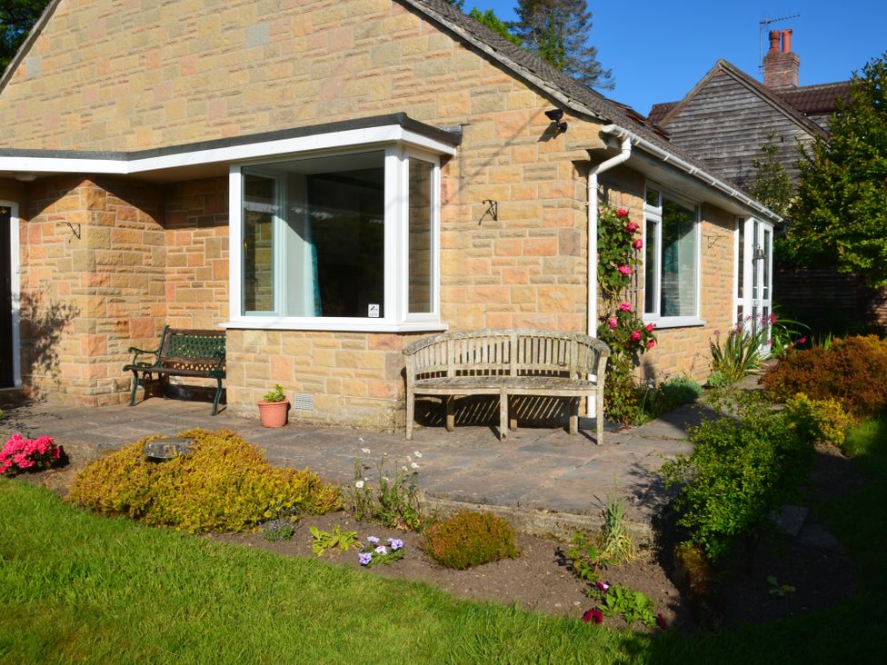 An outdoor patio area with benches and flower beds beside a stone house at Woodstock in Chaffcombe near Chard