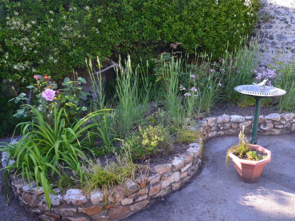 A stone raised flower bed with plants and flowers next to a birdbath and a potted plant in a garden at Woodstock in Chaffcombe near Chard