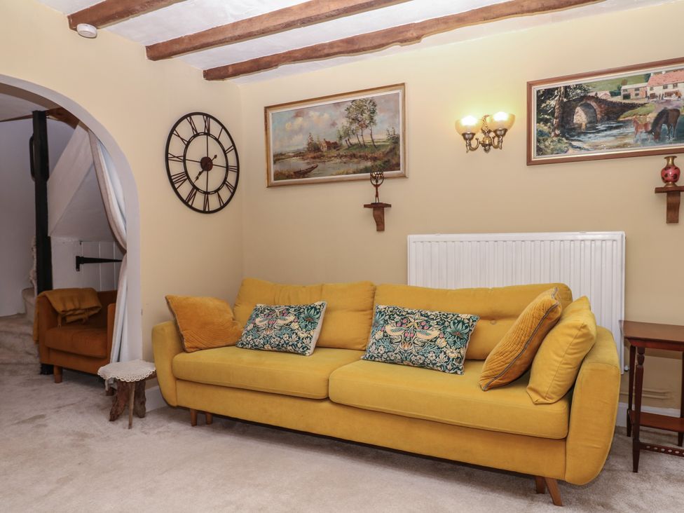 A living room with a yellow sofa and paintings at Mei Cottage in Pinhoe