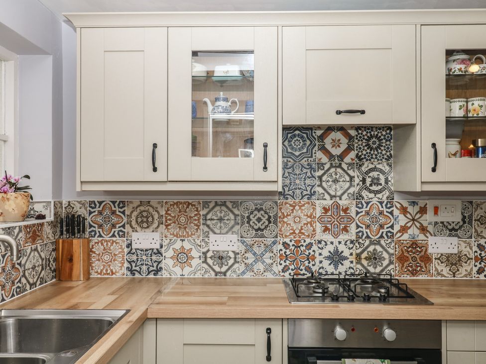 A kitchen with cabinets and decorative tiles at Mei Cottage in Pinhoe