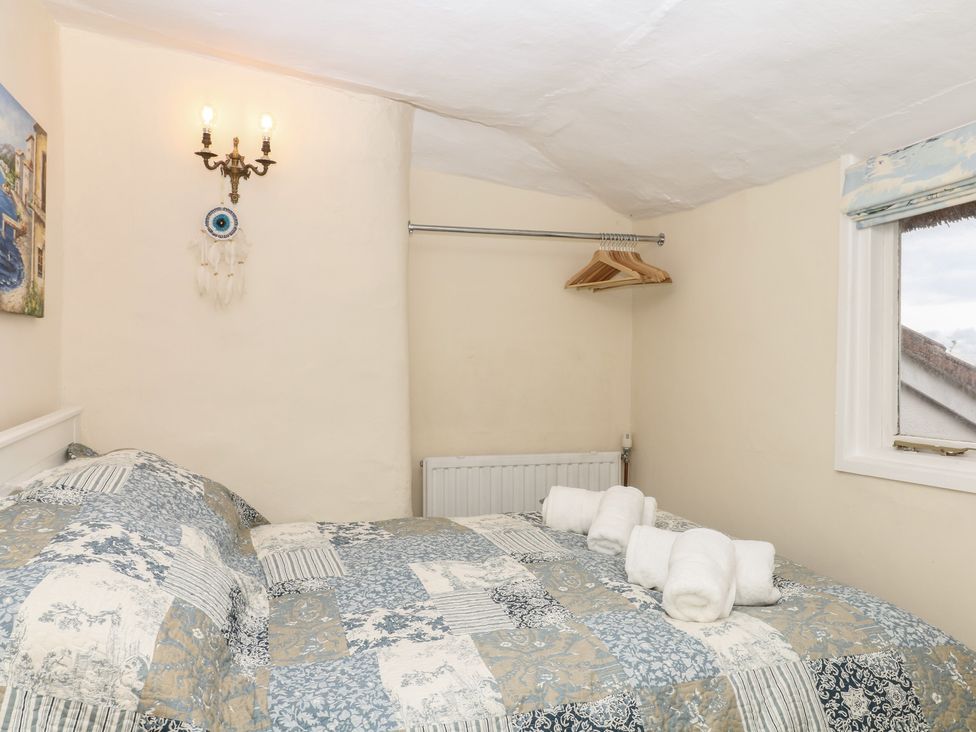 A bedroom with a bed, sconce light, and hangers at Mei Cottage in Pinhoe