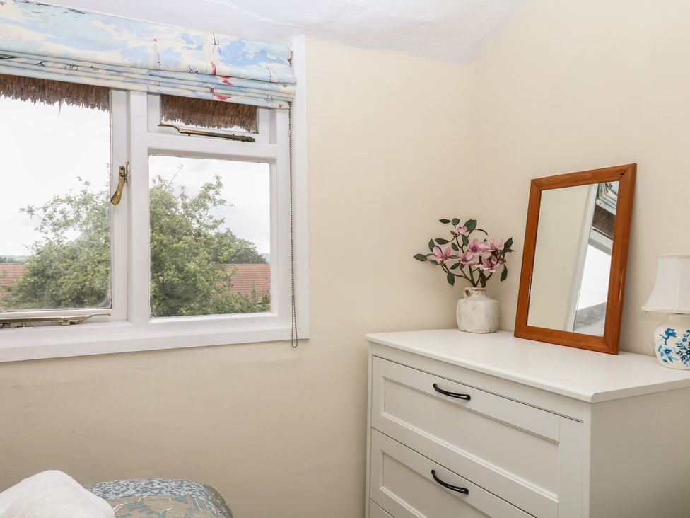 A bedroom with a window and a mirror at Mei Cottage in Pinhoe