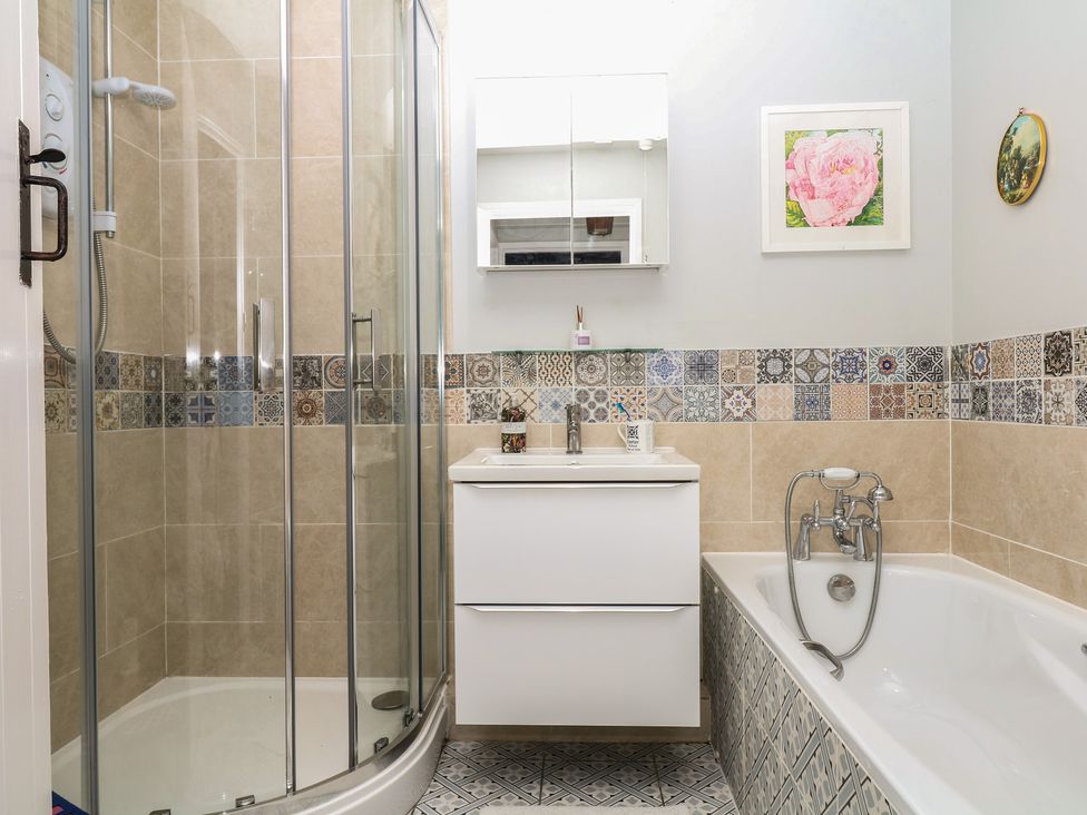A bathroom with a shower, bathtub, and sink at Mei Cottage in Pinhoe