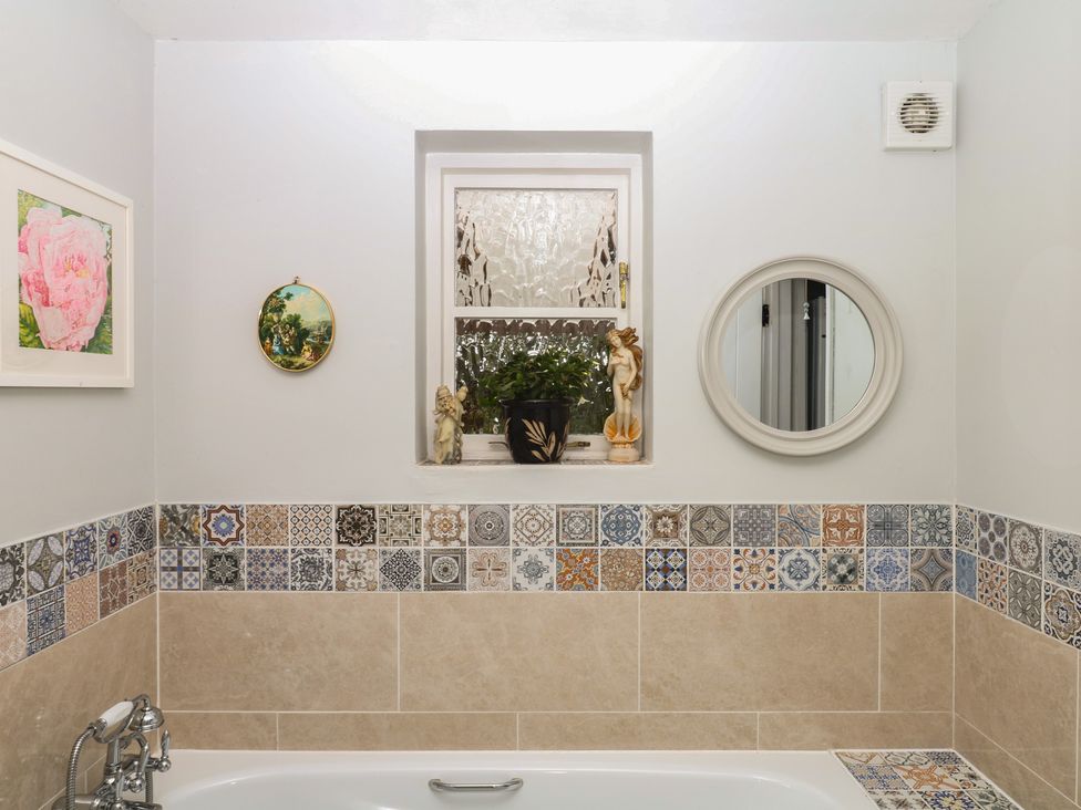 A bathroom with decorative tiles and a mirror at Mei Cottage in Pinhoe