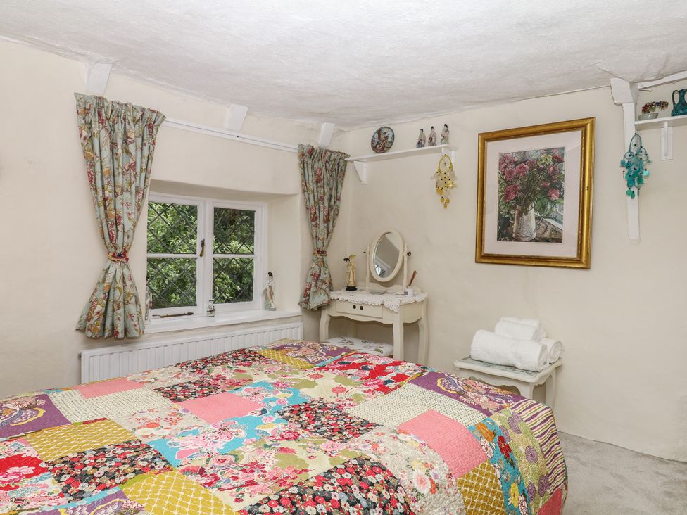 A bedroom with a quilted bed and a dressing table at Mei Cottage in Pinhoe
