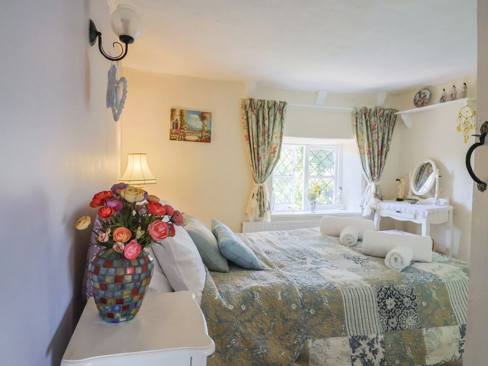 A bedroom with a bed, vase of flowers and mirror at Mei's Cottage in Pinhoe