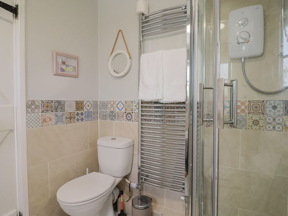 A bathroom with a toilet, shower, and towel rail at Mei's Cottage in Pinhoe