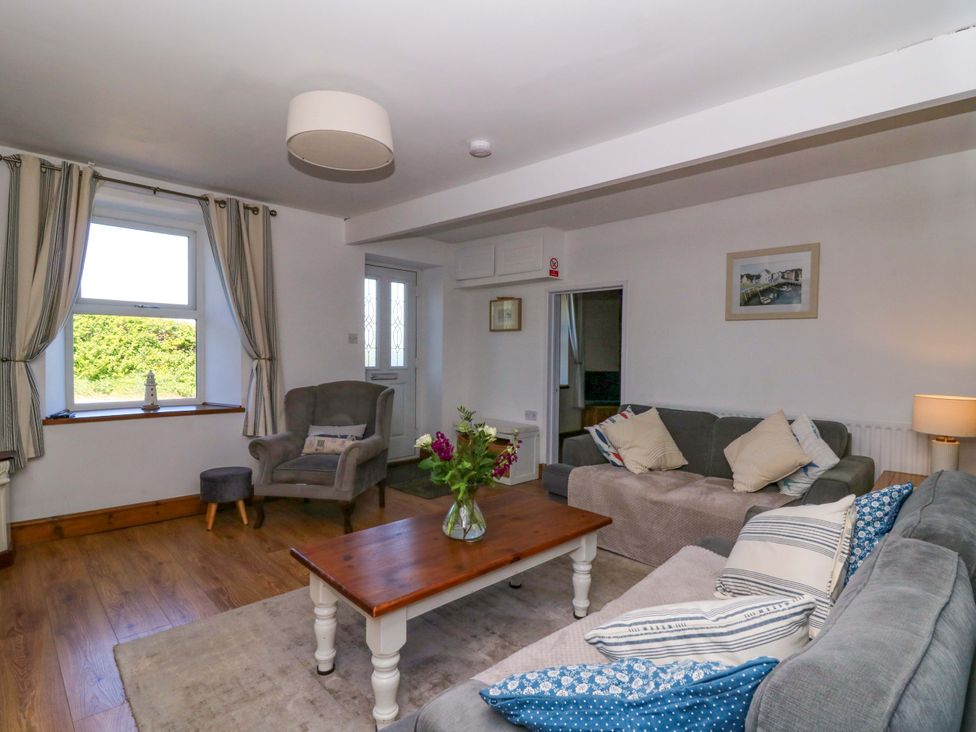 A living room with sofas, cushions, armchair, coffee table with flowers, window with curtains and door at Towyn Hall in New Quay