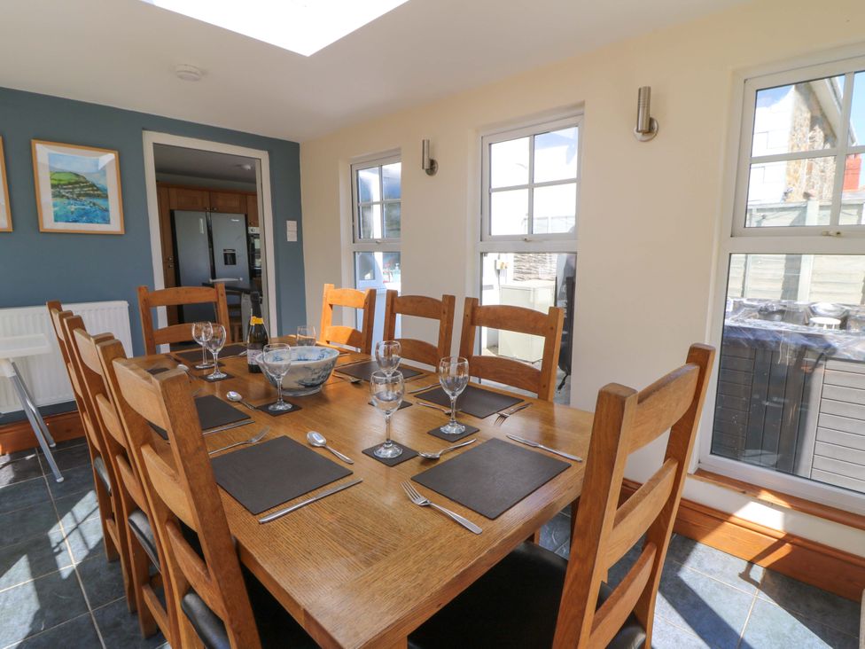 A dining room with a wooden table and eight chairs set with placemats, cutlery, and glassware with windows letting in natural light at Towyn Hall in New Quay