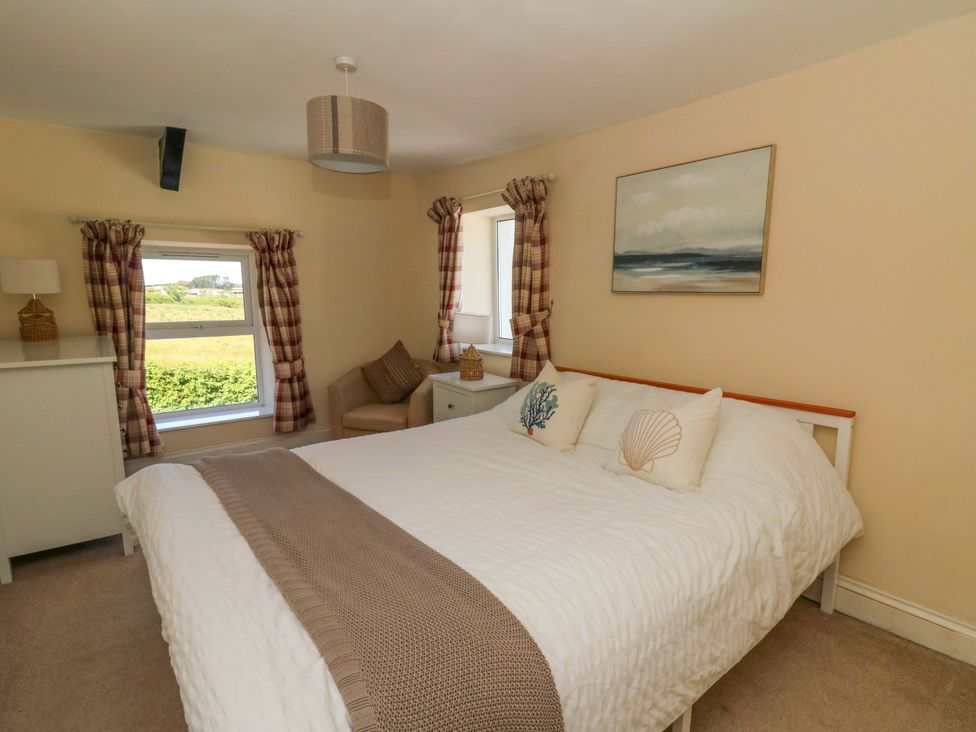 A bedroom with a bed white bedding pillows nightstand sweater armchair lamps windows and wall art at Towyn Hall in New Quay