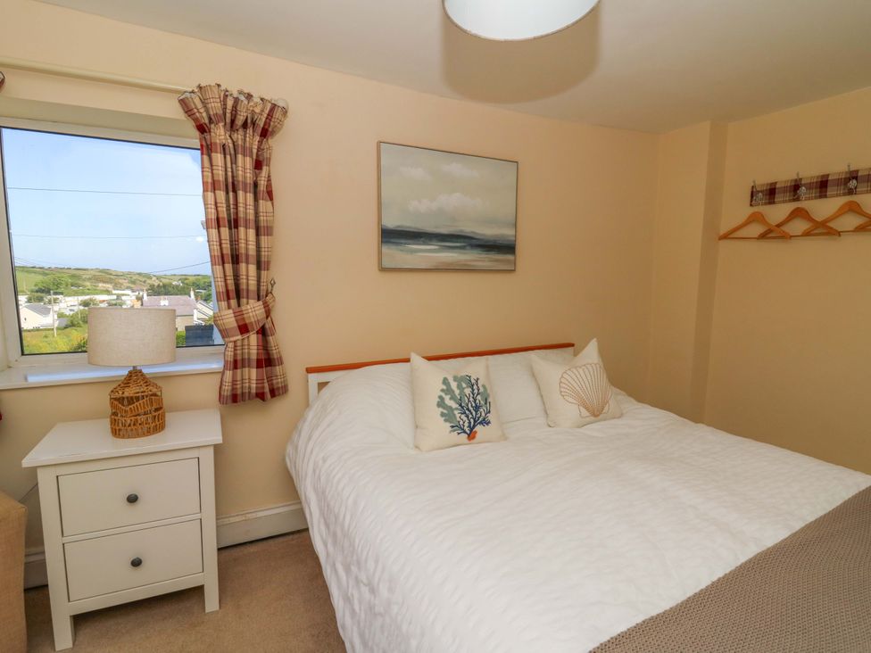 A bedroom with a bed with white bedding and decorative pillows a nightstand with a lamp and a window with plaid curtains at Towyn Hall in New Quay