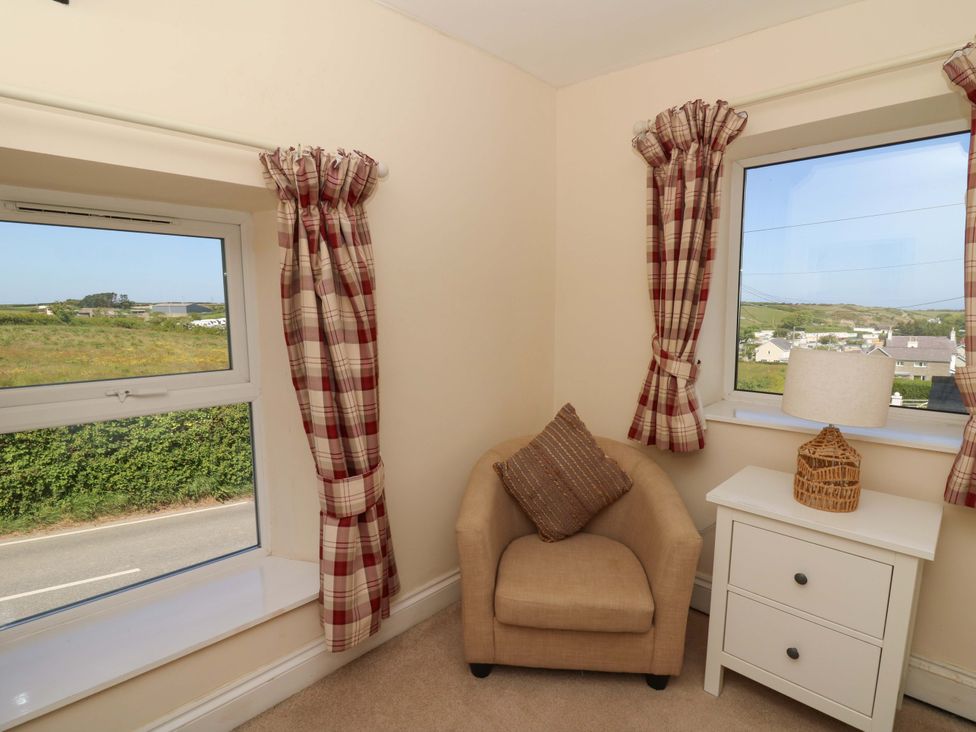 A corner with a beige armchair, a cushion, two windows with red plaid curtains, and a white bedside table with a lamp at Towyn Hall in New Quay