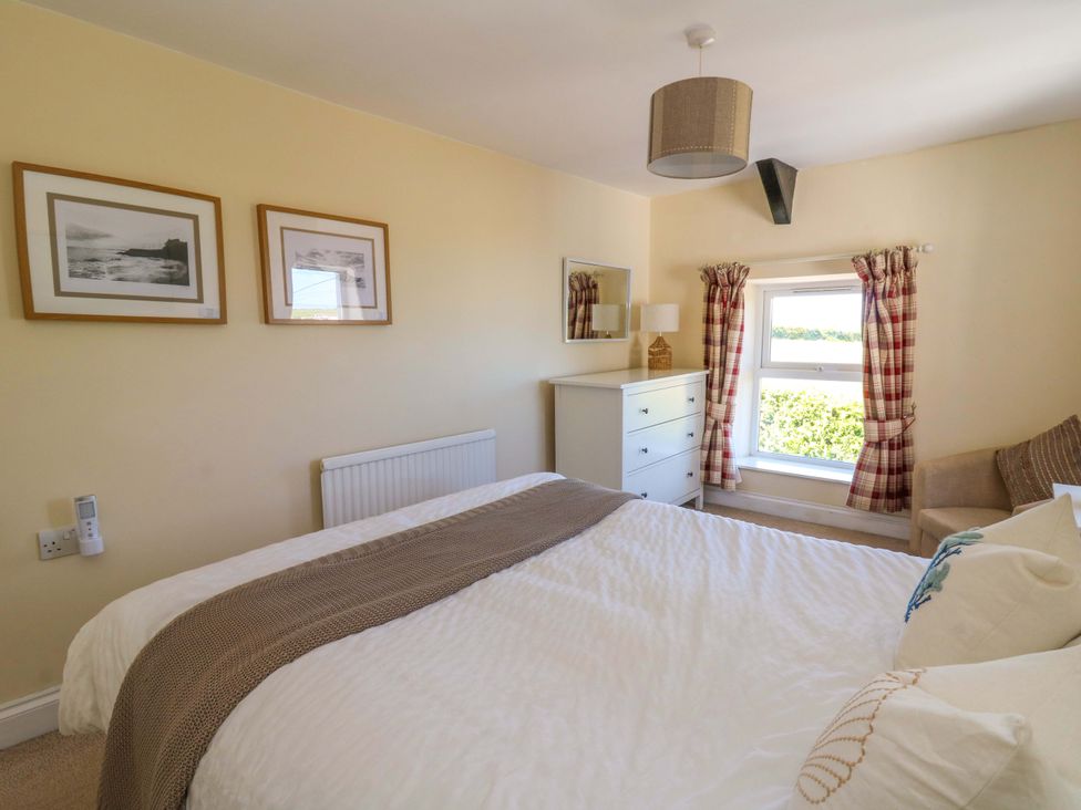 A bedroom with a bed pillows a dresser a lamp two framed pictures and a window with curtains at Towyn Hall in New Quay