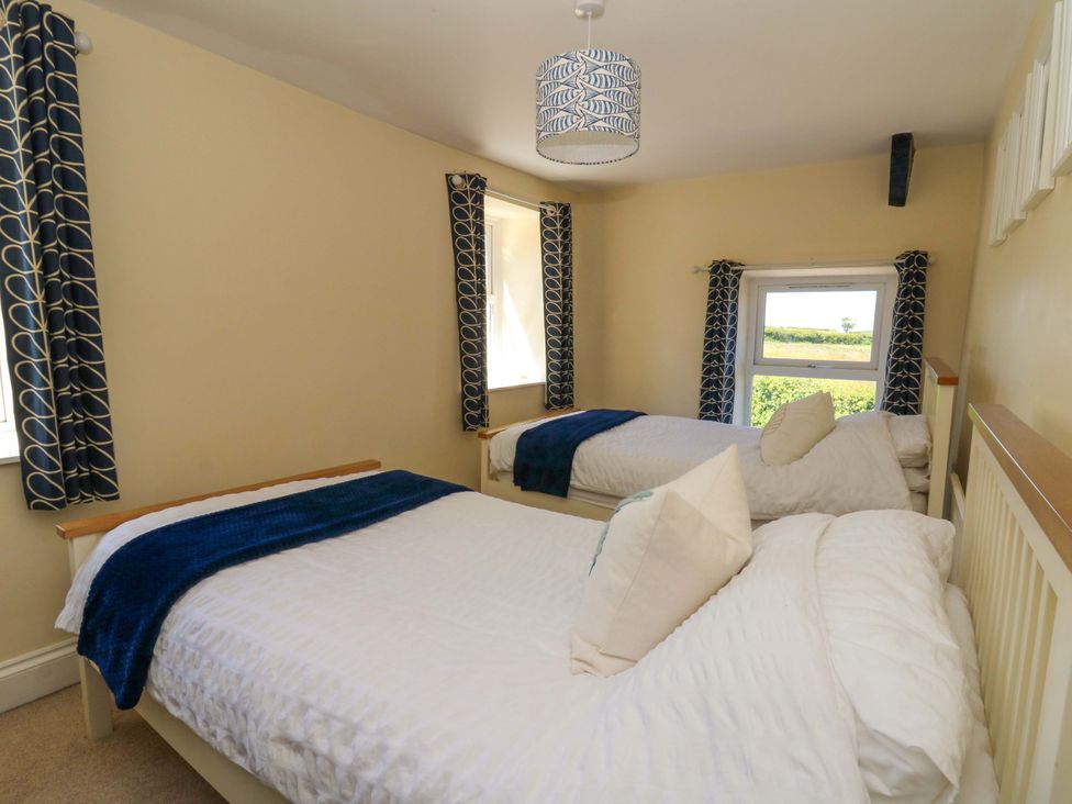 A bedroom with two single beds with white bedding and blue throws next to windows with blue patterned curtains at Towyn Hall in New Quay