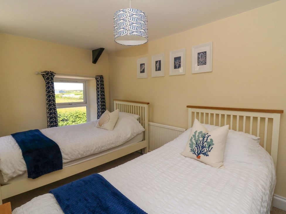 A bedroom with two single beds white bedding blue throws and a window with patterned curtains at Towyn Hall in New Quay