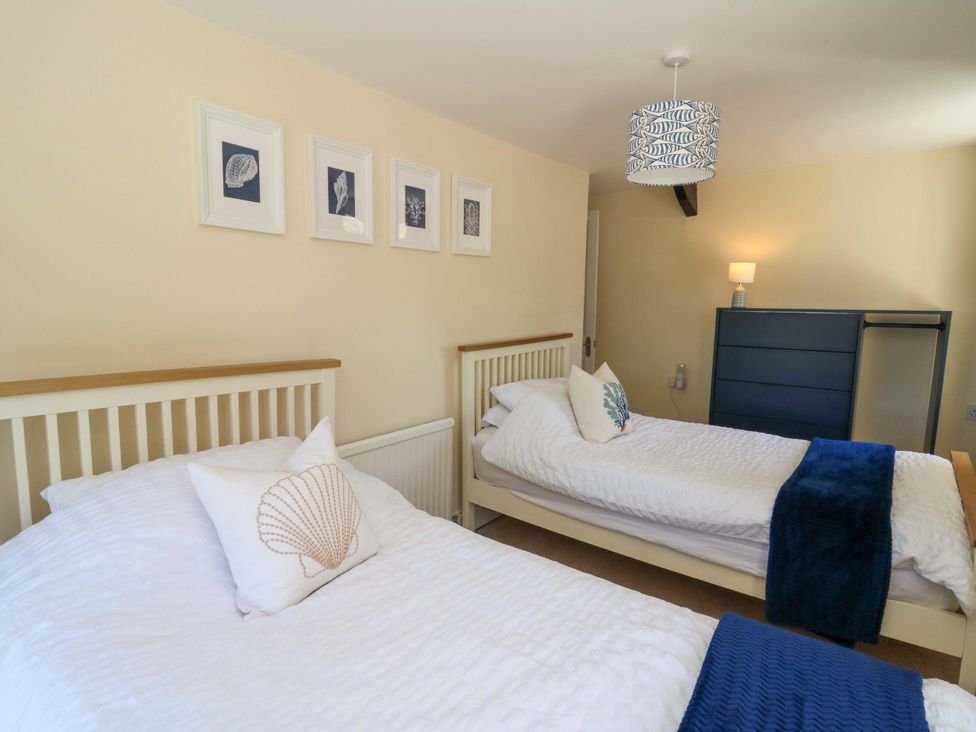 A bedroom with two single beds white bedding cushions framed pictures and a chest of drawers at Towyn Hall in New Quay