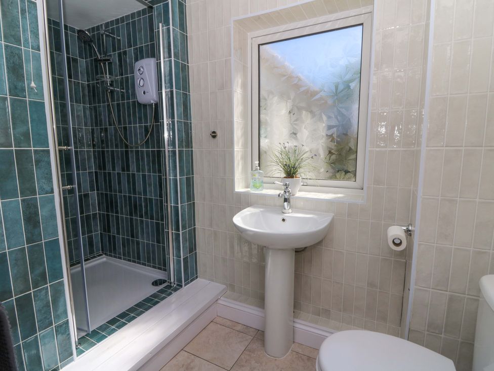 A bathroom with a shower, pedestal sink, frosted window with plant, and toilet at Towyn Hall in New Quay