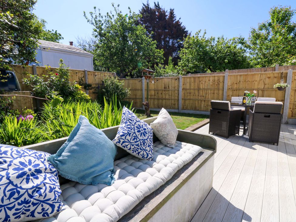 A garden patio with a cushioned bench with patterned pillows and a dining table with chairs at Towyn Hall in New Quay
