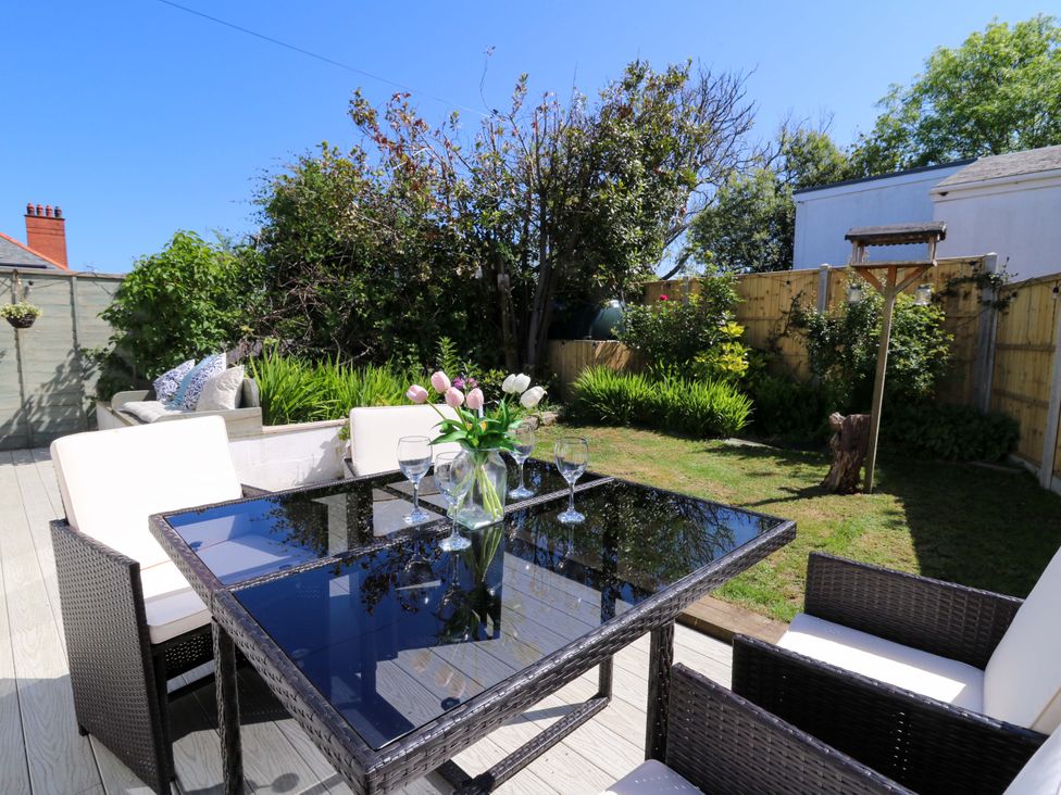 An outdoor patio with a glass top table and wicker chairs next to a garden with grass and plants at Towyn Hall in New Quay