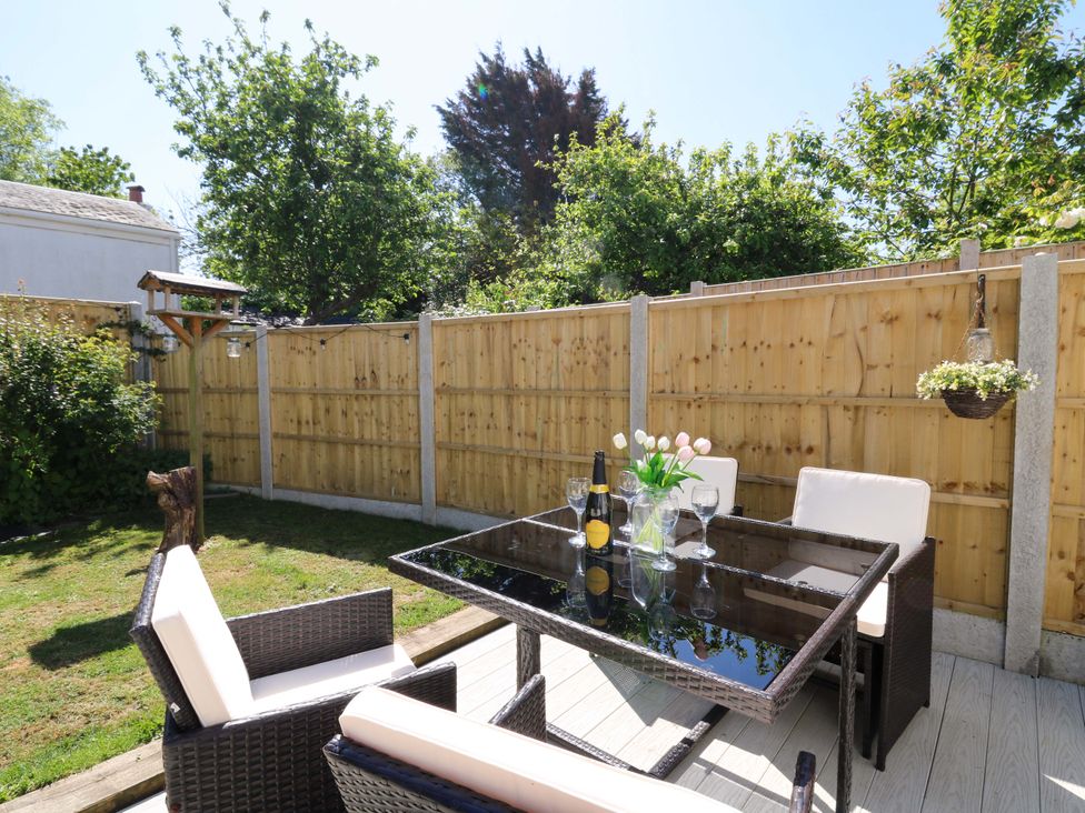 An outdoor patio with a glass table and four chairs with cushions wine bottle and glasses on the table at Towyn Hall in New Quay