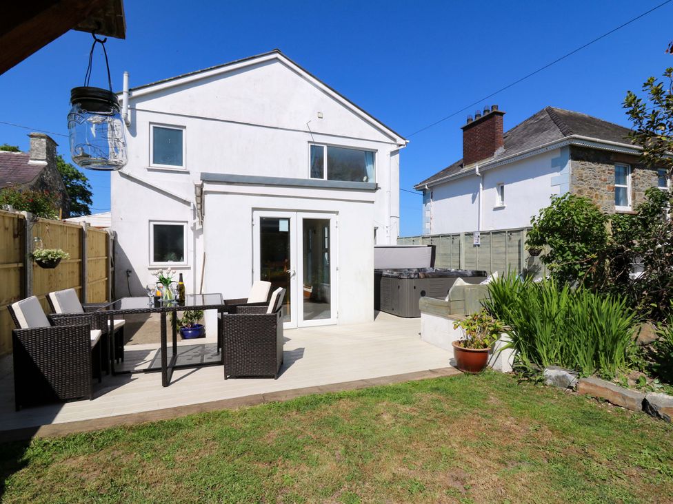 A backyard patio with outdoor furniture a dining table chairs a hot tub and plants at Towyn Hall in New Quay