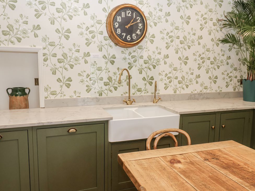 A kitchen with a sink, clock, and wooden table at Syleham House in Syleham near Eye