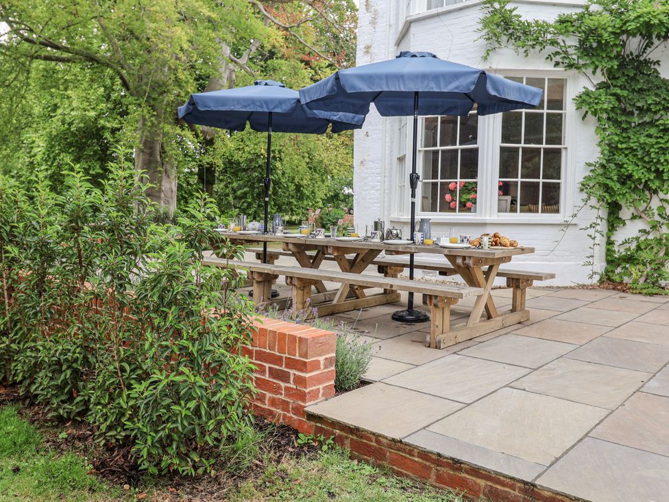An outdoor dining area with a wooden table and umbrellas at Syleham House Syleham near Eye