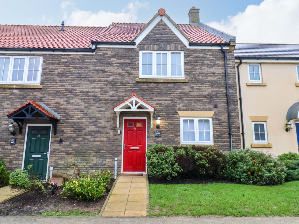 A house with a red front door and green bushes at The Beach Retreat The Bay - Filey