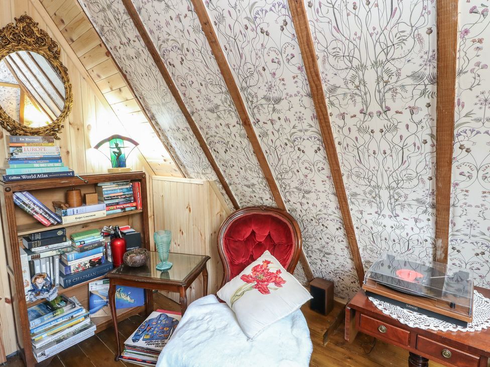 A reading nook with a bookshelf and an armchair at The Cottage In The Woods, Connel, Argyll & Bute