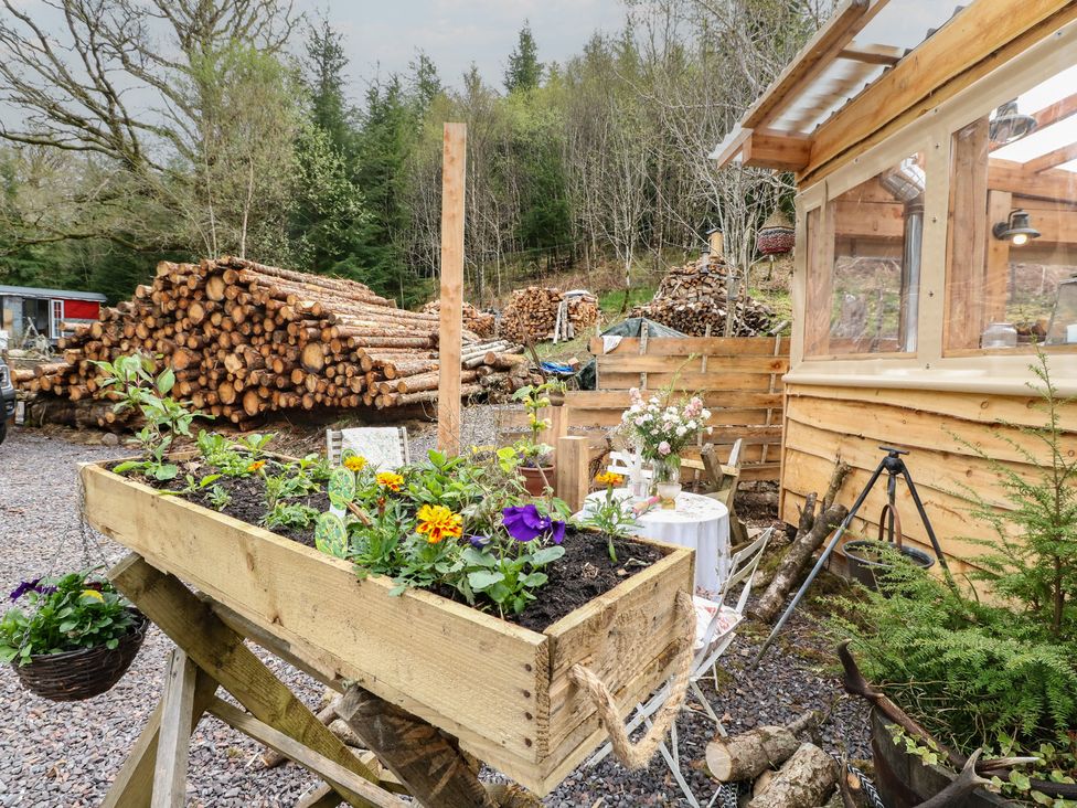 An outdoor area with a flower bed and wood logs at The Cottage In The Woods in Connel, Argyll & Bute