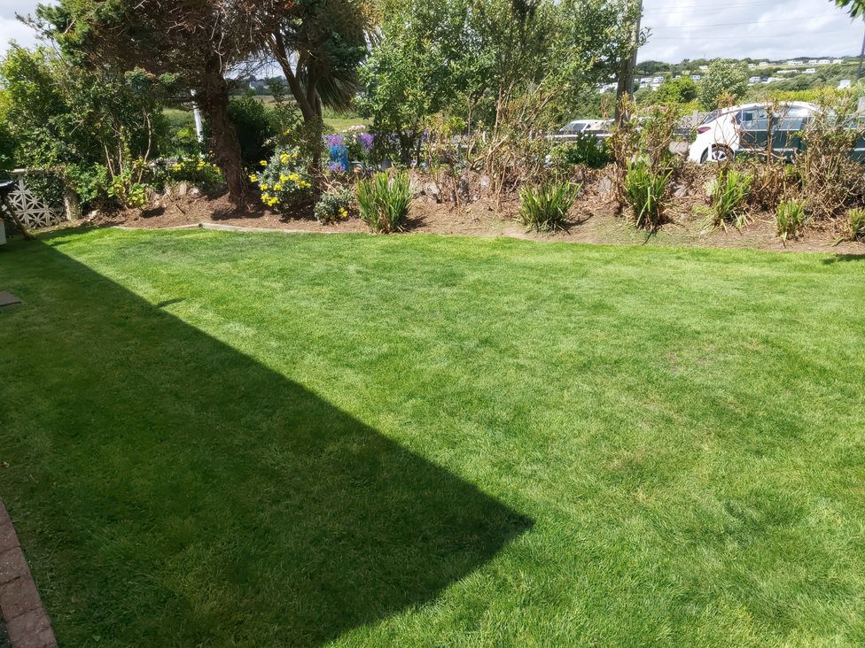 A garden with a lawn and flower beds at Llwyn Eithin in Benllech