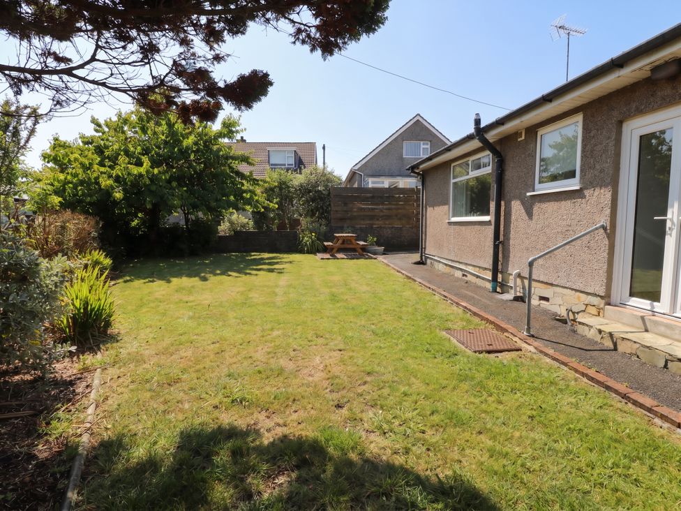 A garden with grass and a wooden bench at Llwyn Eithin in Benllech