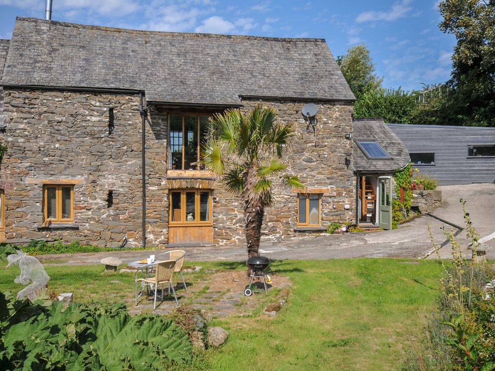 A stone building with a palm tree and outdoor seating at Little Coombe in Trehunist near Liskeard