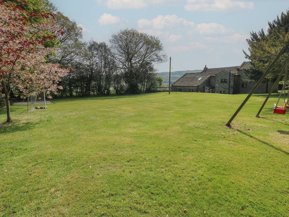 An outdoor area with a house, swing, and grassy field at Stagwood House in New Mill