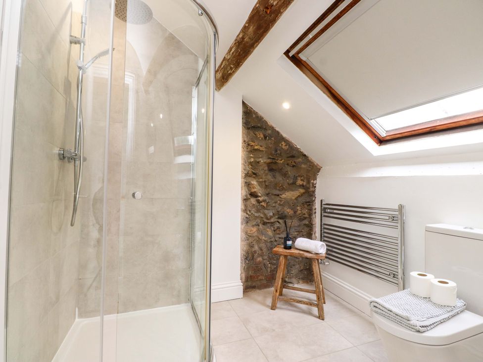 A bathroom with a shower, toilet, radiator, and wooden stool at Hendre in Menai Bridge