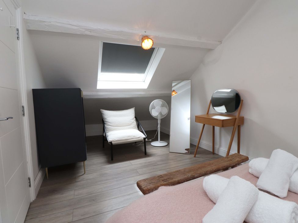 A bedroom with a bed, towels, chair, fan, and wardrobe at Hendre in Menai Bridge