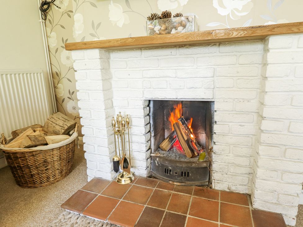 A fireplace with logs burning and a basket of firewood at Lake View Cottage Well near Alford
