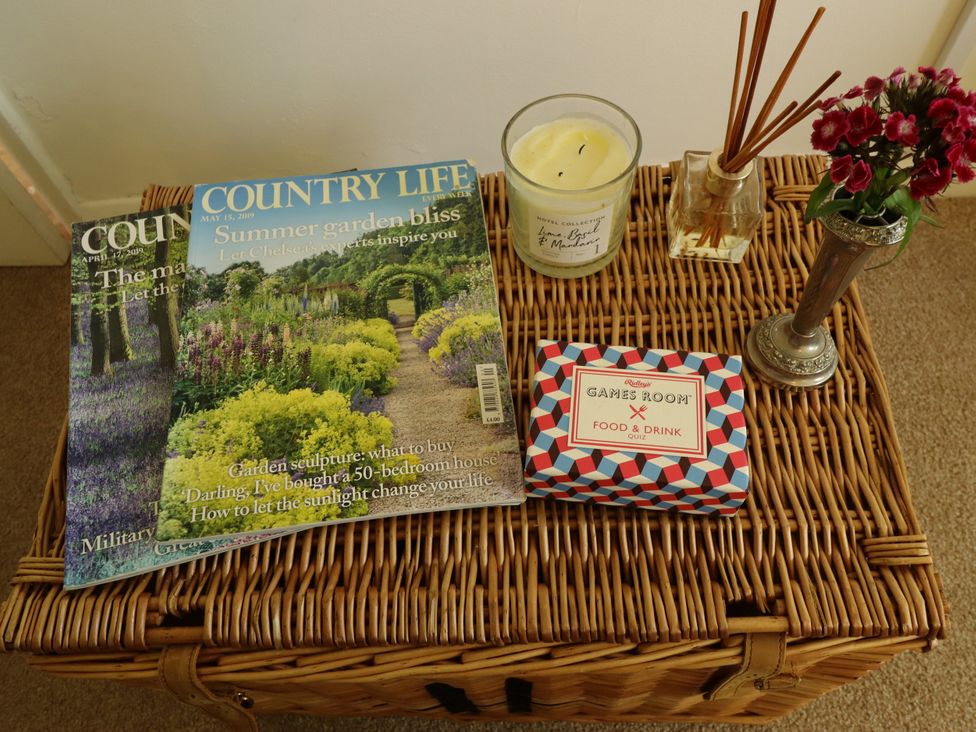 A living room with magazines and a candle on a wicker storage box at Lake View Cottage in Well near Alford