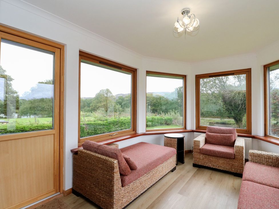 A conservatory with seating and windows at Maybank in Muirshearlich