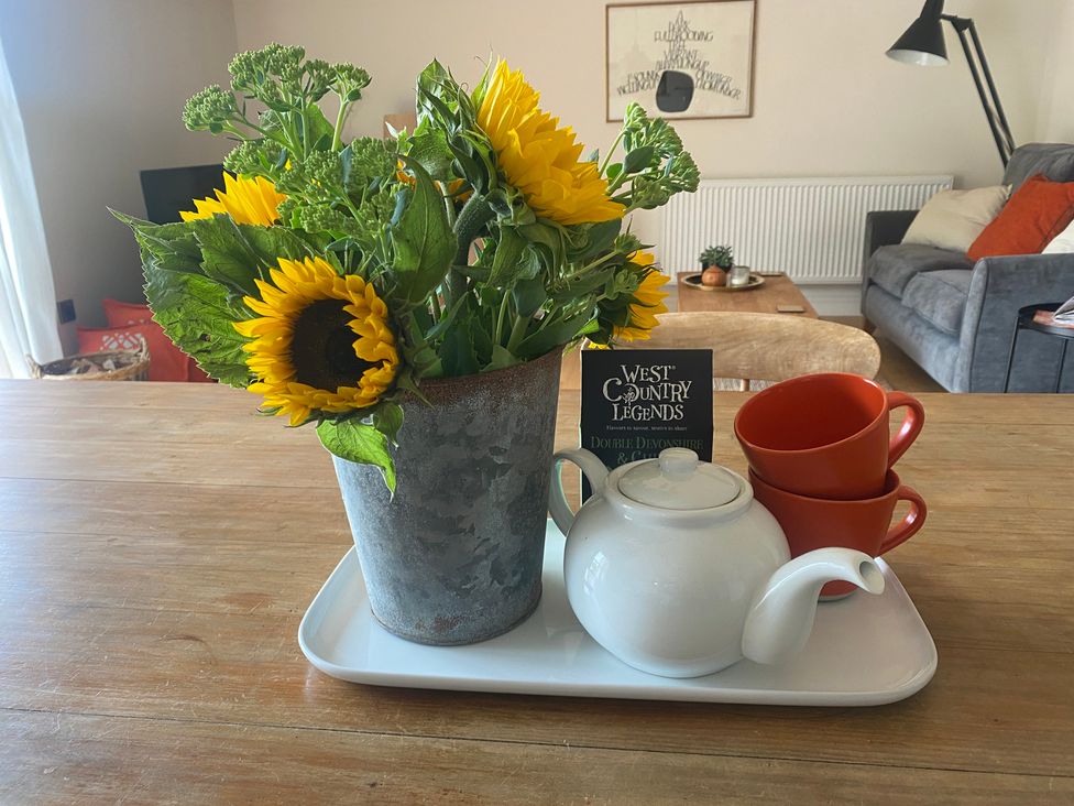 A tray with sunflowers in a pot, a teapot, red cups and a book in a living room at Church Farm Dairy Cadbury near Thorverton