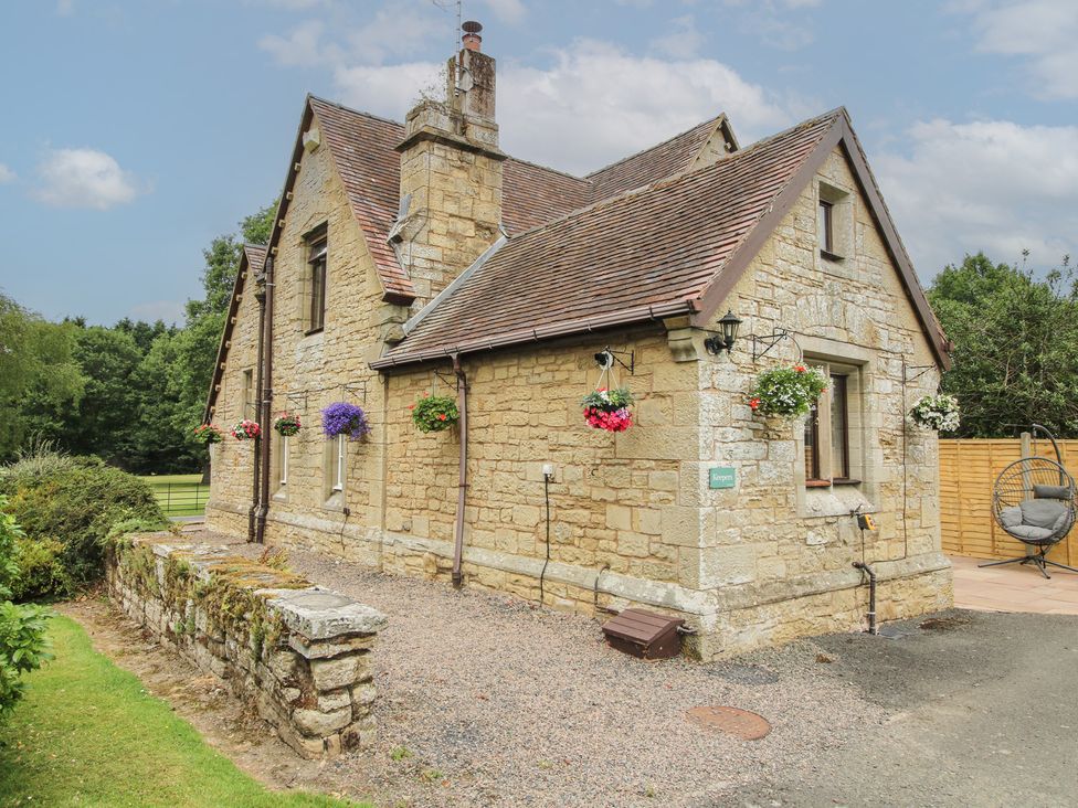 A stone house with hanging baskets and gravel pathway at Keepers Cottage in Shobdon