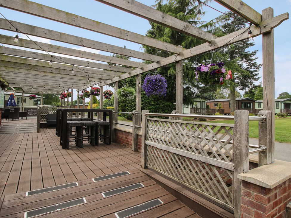 An outdoor seating area with a wooden pergola and flower baskets at Keepers Cottage in Shobdon