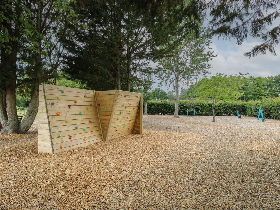 A climbing wall in a playground surrounded by trees at Keepers Cottage Shobdon