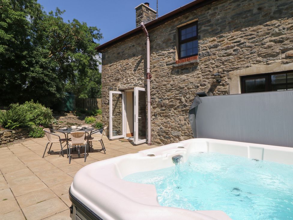 An outdoor patio with a hot tub and table with chairs at Felin Gogoyan Tregaron