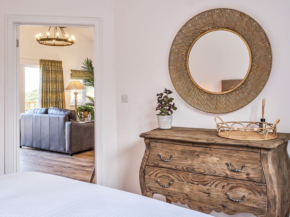 A bedroom with a wooden dresser and a mirror at Heritage Retreat in Monknash